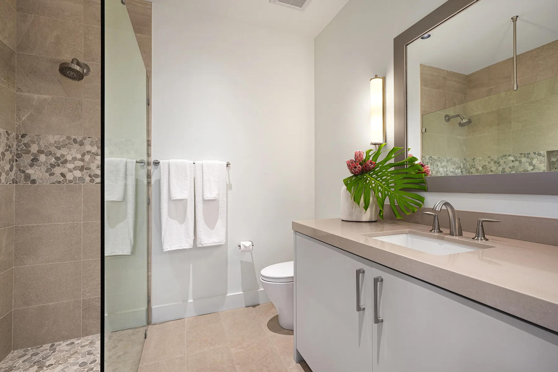 A bright bathroom with a glass shower, sink, and towels hanging on the wall.