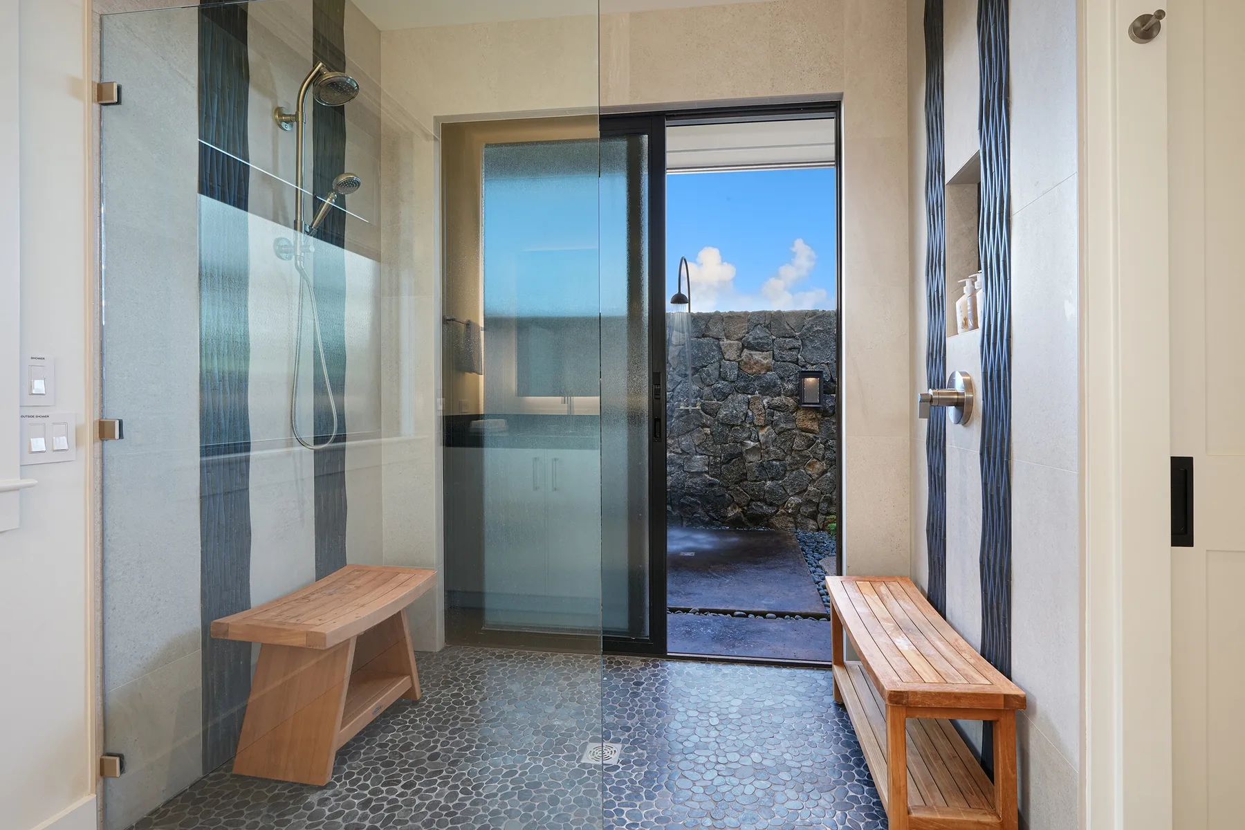 A tiled bathroom has a glass shower enclosure and a doorway opening onto a stone-walled outdoor area.