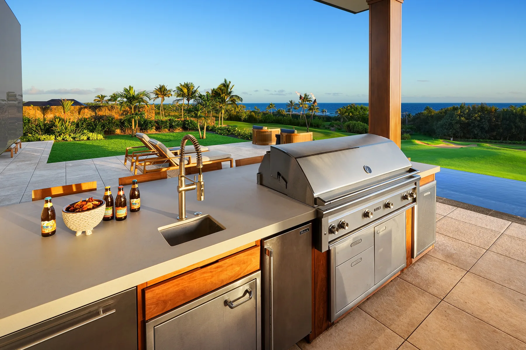 An outdoor kitchen with a built-in grill overlooks a landscaped lawn and the ocean.