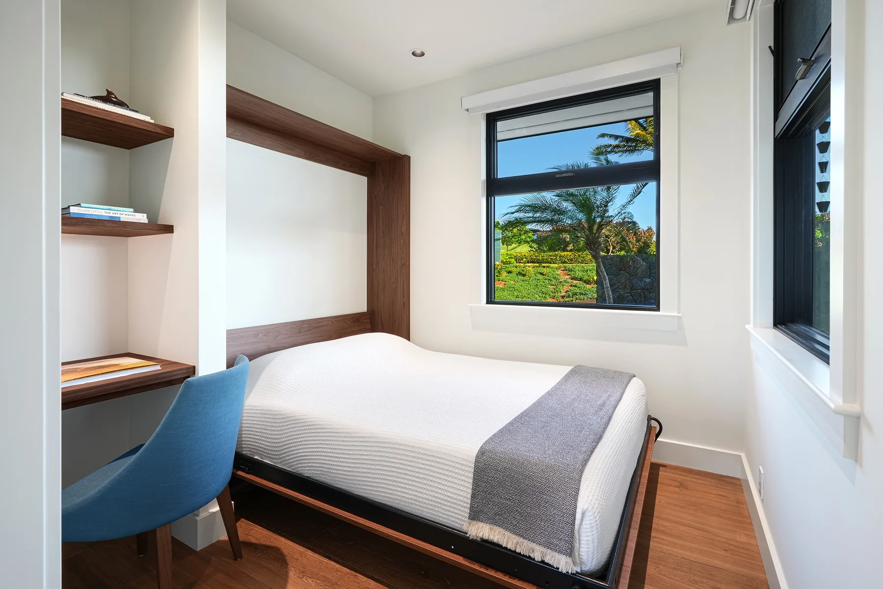 A bedroom with a neatly made bed and a window overlooking greenery.