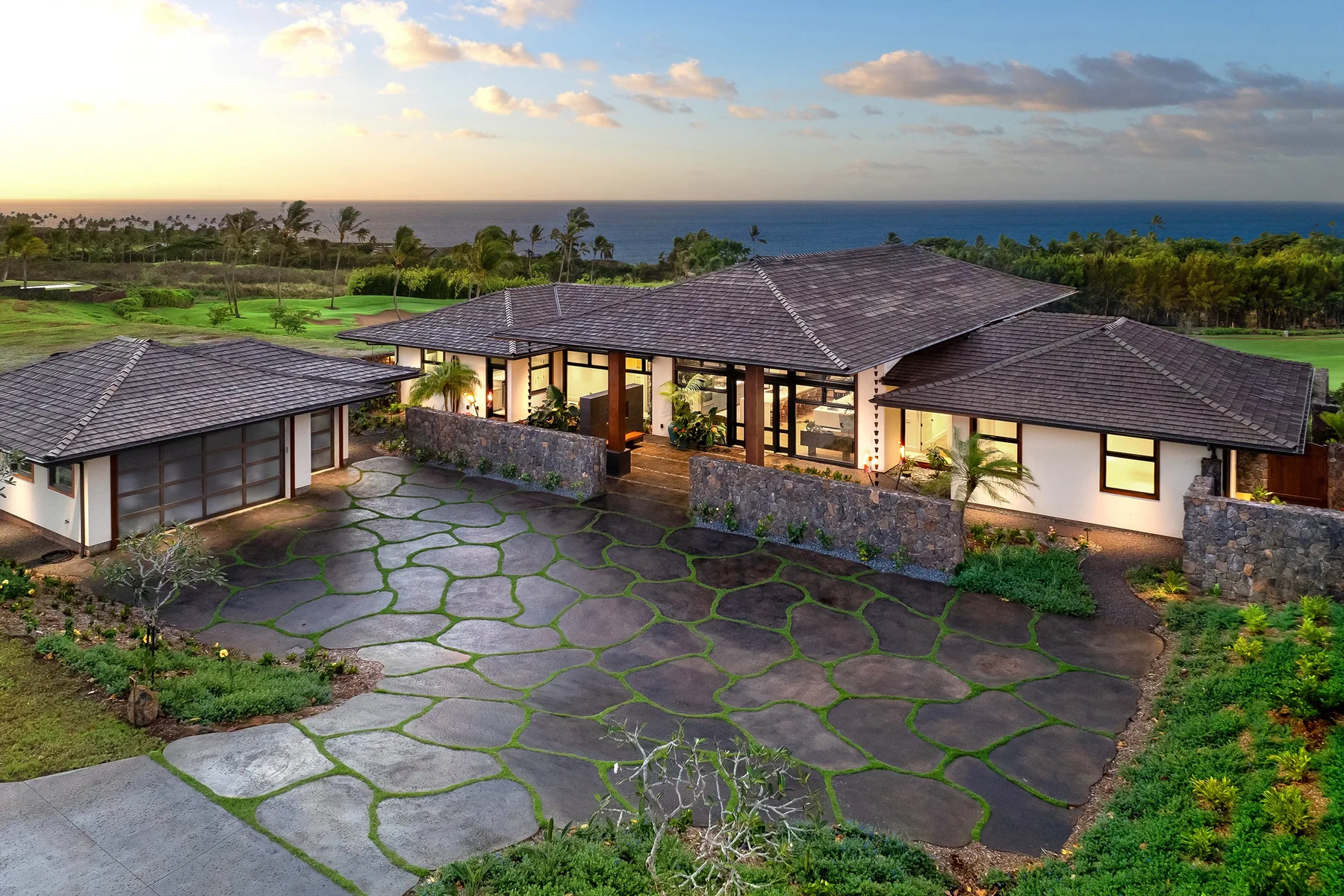 A sprawling single-story house overlooks a landscaped driveway and the ocean.