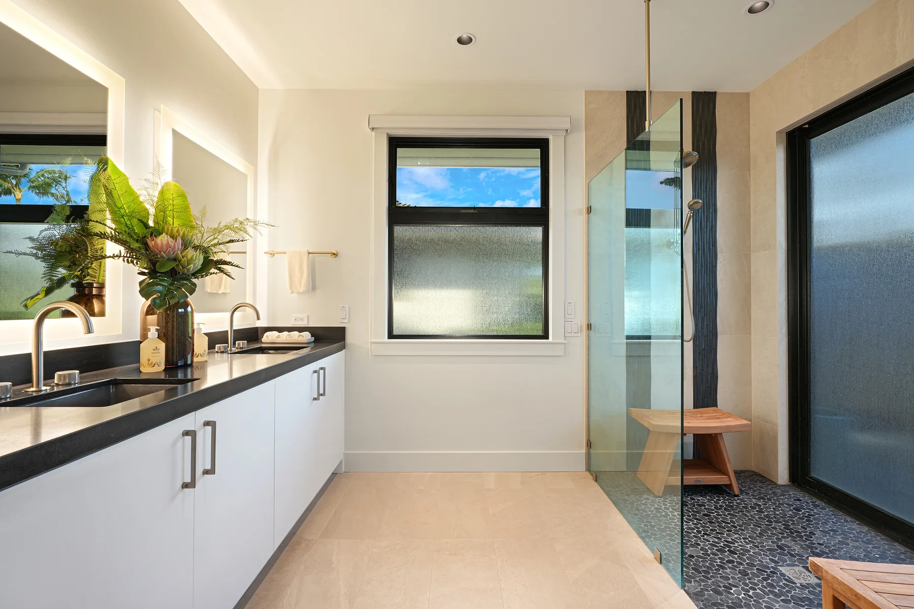 A bright bathroom with a long vanity, a window, and a glass shower.