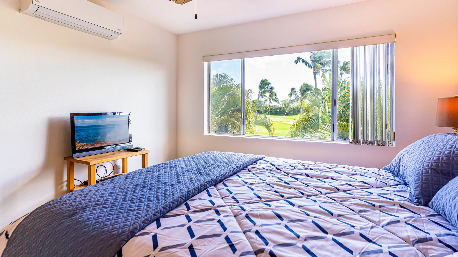 A bedroom with patterned bedding and a large window overlooking palm trees.