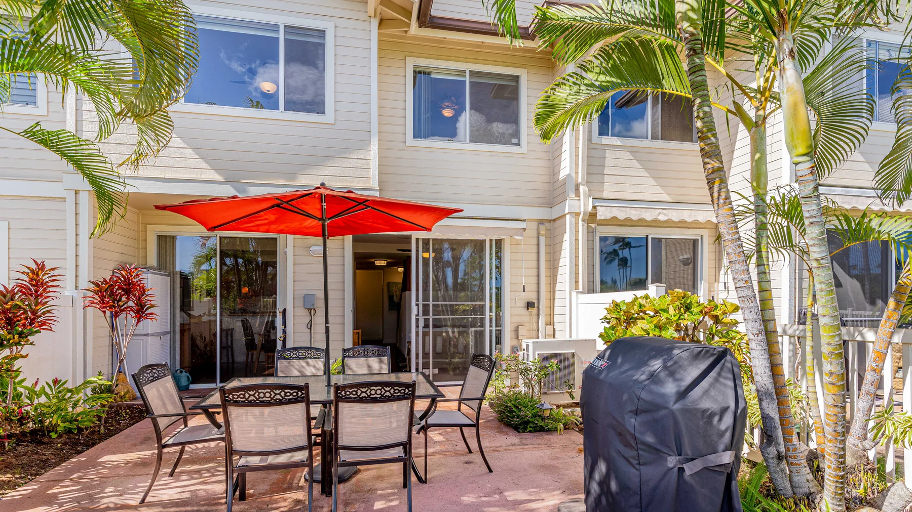An outdoor patio with a dining table and red umbrella beside a light-colored building.