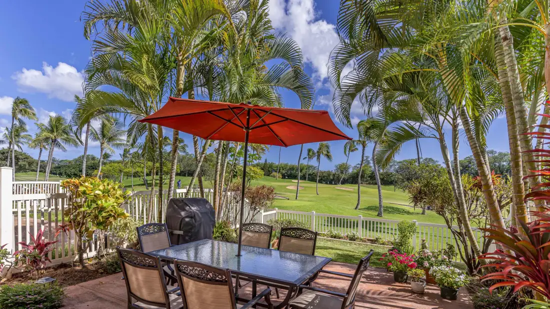 A patio dining area with a table and red umbrella overlooks a green landscape.