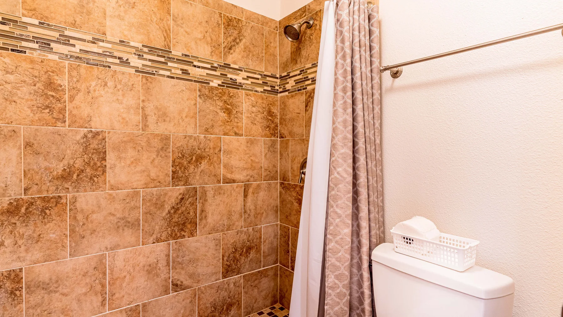A tiled bathroom shower with a patterned curtain beside a toilet.