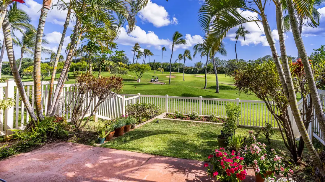 A landscaped garden patio opens onto a broad green lawn beneath palm trees.