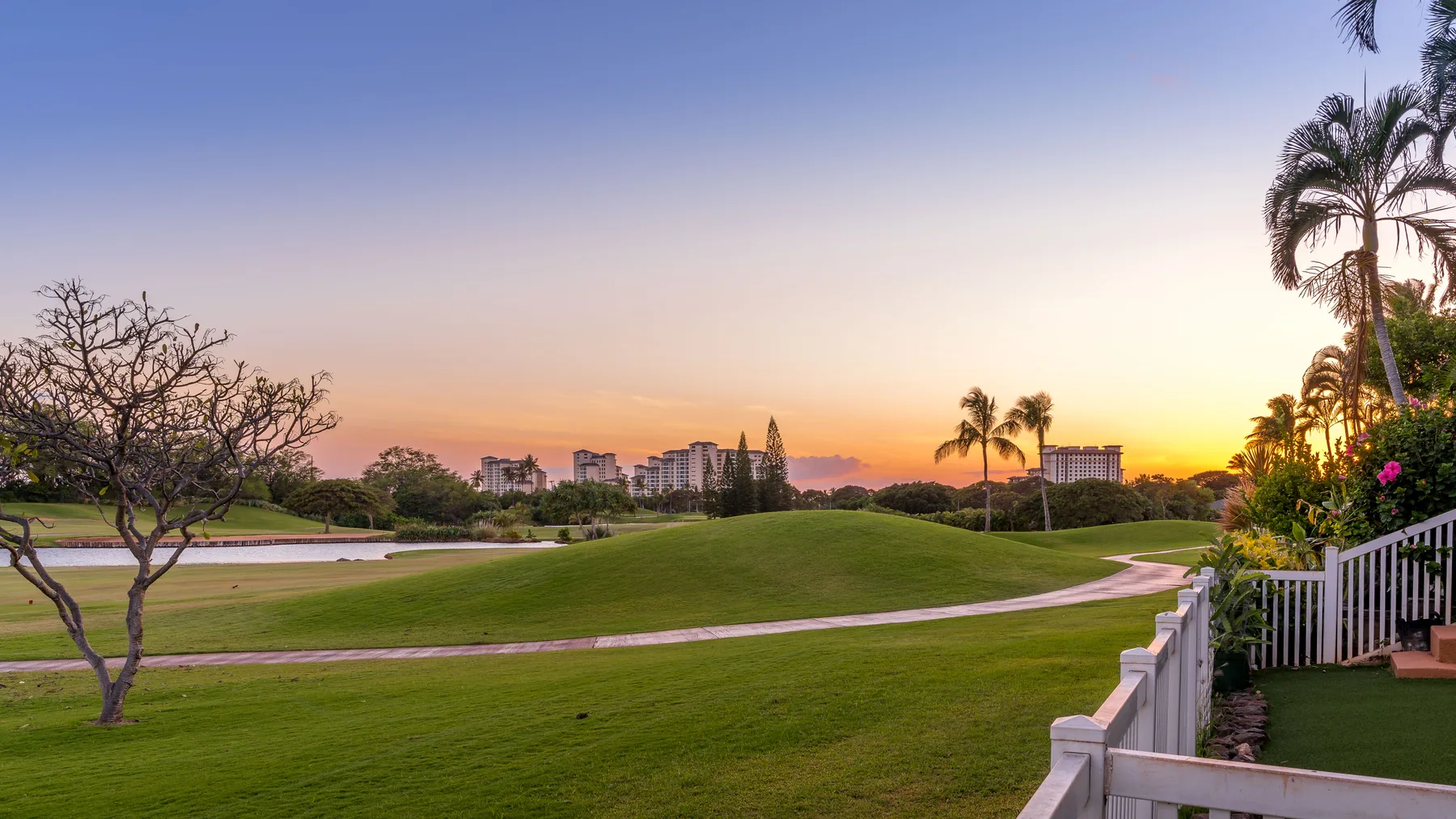 A landscaped golf course with a winding path beneath a colorful sunset sky.