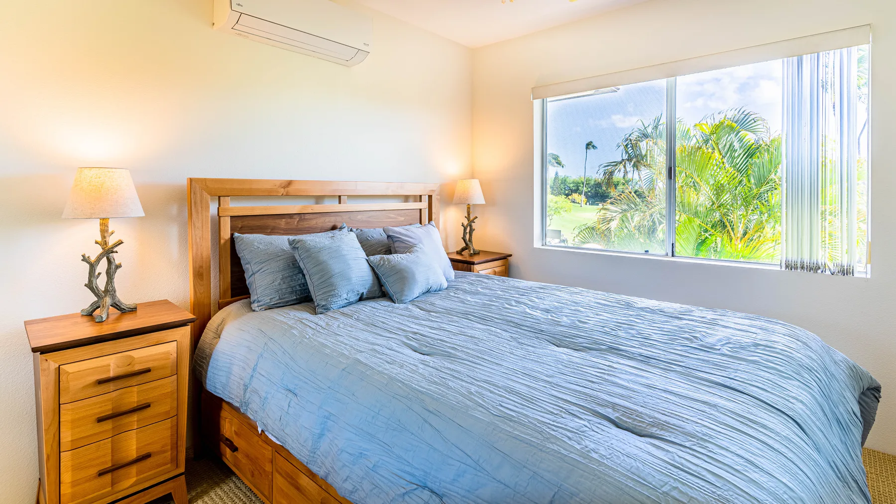 A bedroom with a wooden bed, blue bedding, and a large window overlooking greenery.
