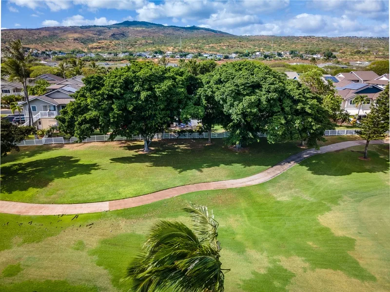 A green park with a winding path and trees, with homes and hills in the distance.