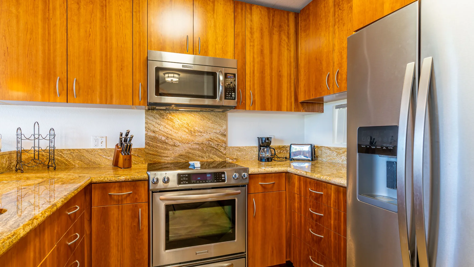 A kitchen with wooden cabinets, stainless steel appliances, and stone countertops.