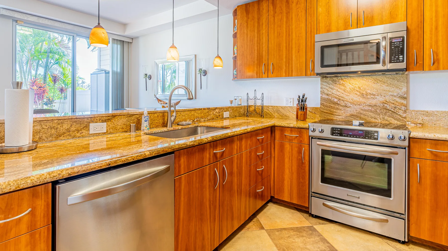 A bright kitchen with wooden cabinets, stone counters, and stainless-steel appliances.