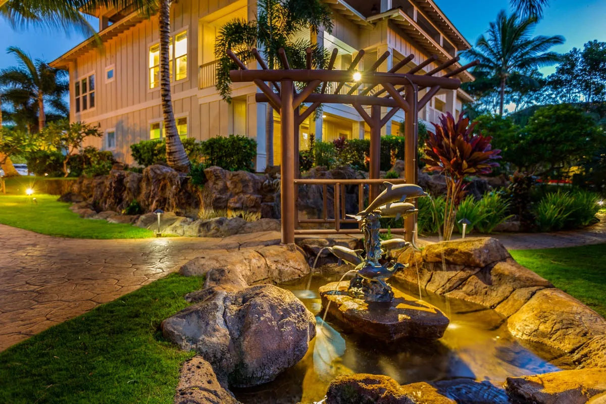 Un estanque ajardinado con rocas y una pérgola de madera junto a un edificio iluminado.
