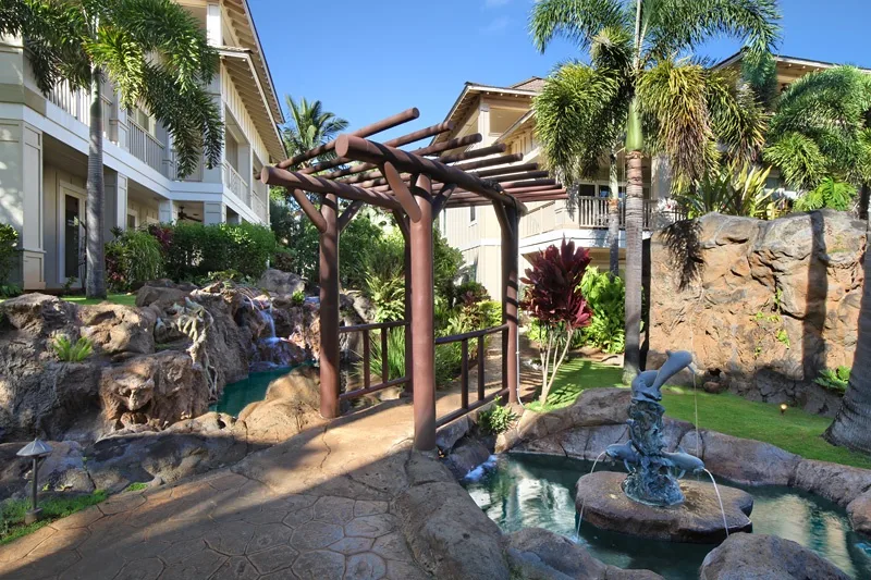 Un patio ajardinado presenta una pérgola de madera, rocas y un pequeño estanque.