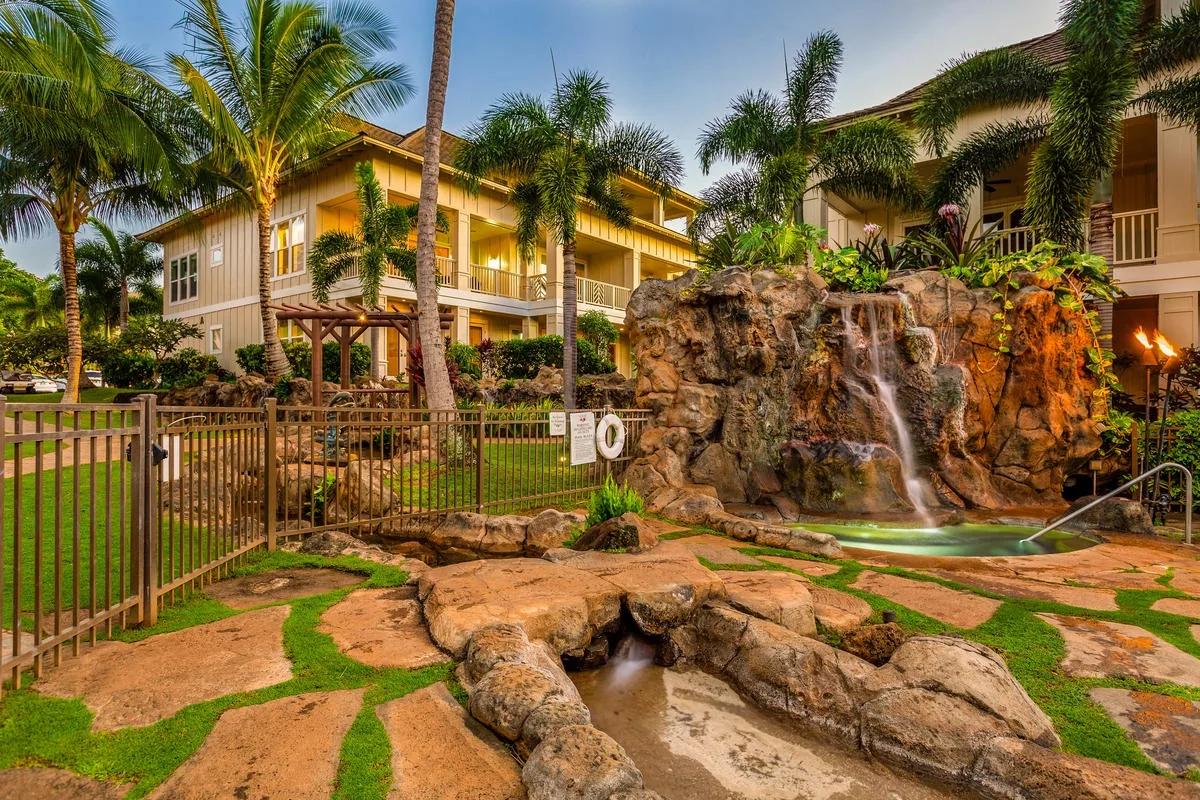 Un patio tropical presenta una cascada rocosa rodeada de palmeras.