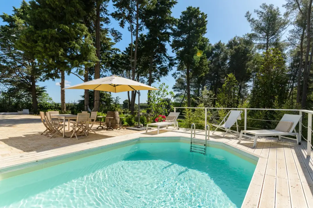 Una piscina al aire libre está junto a una terraza con tumbonas y una zona de comedor.