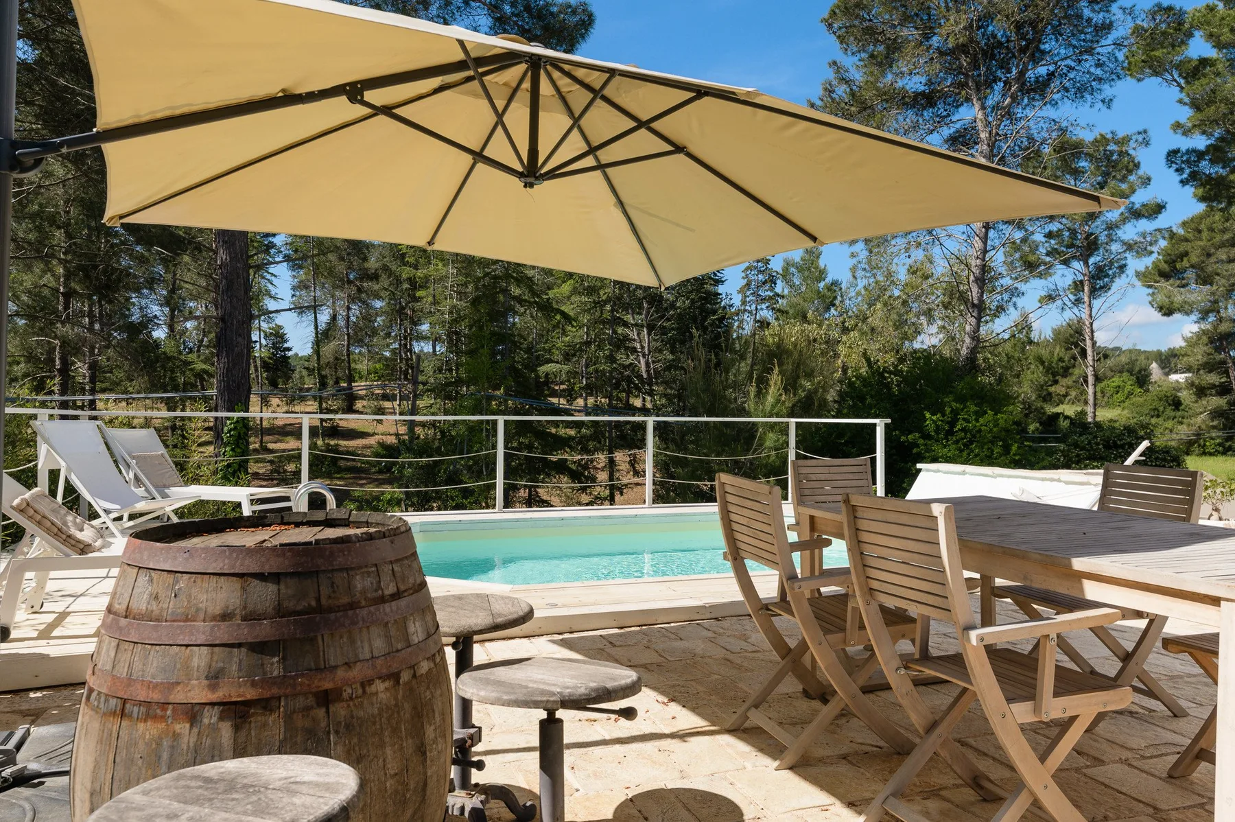 Un patio de piscina al aire libre con una gran sombrilla y asientos de madera.