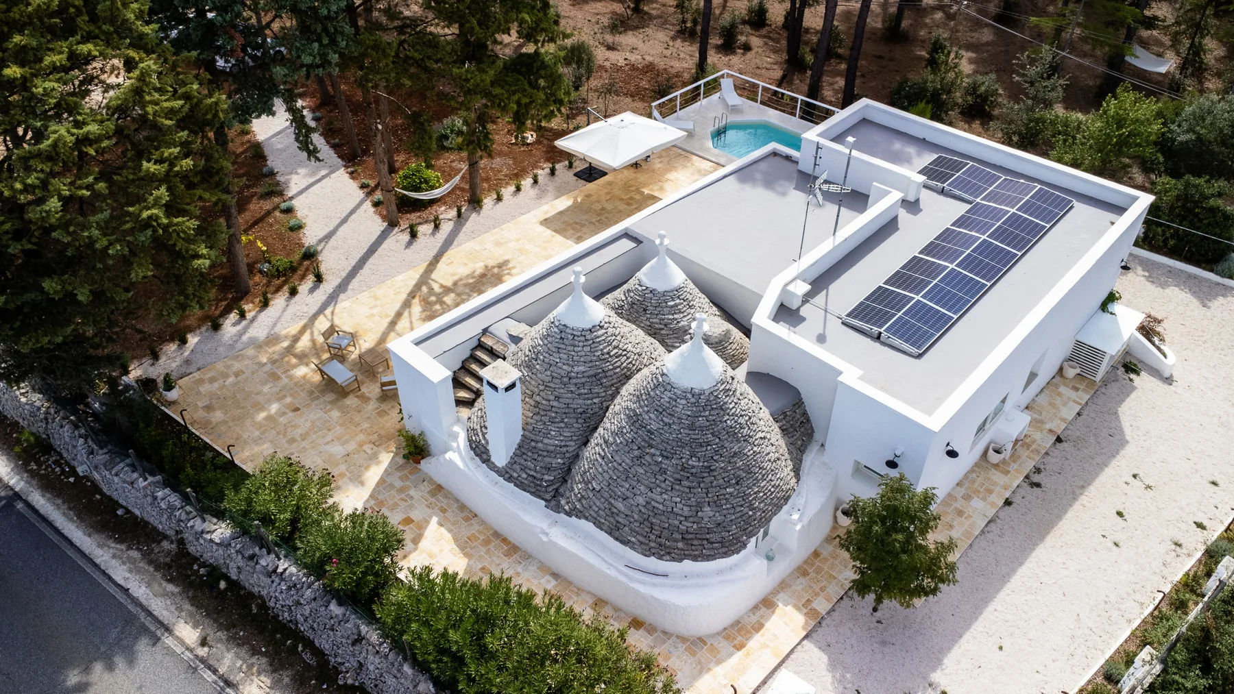 Vista aérea de un edificio blanco con techos abovedados de piedra, paneles solares y una pequeña piscina.