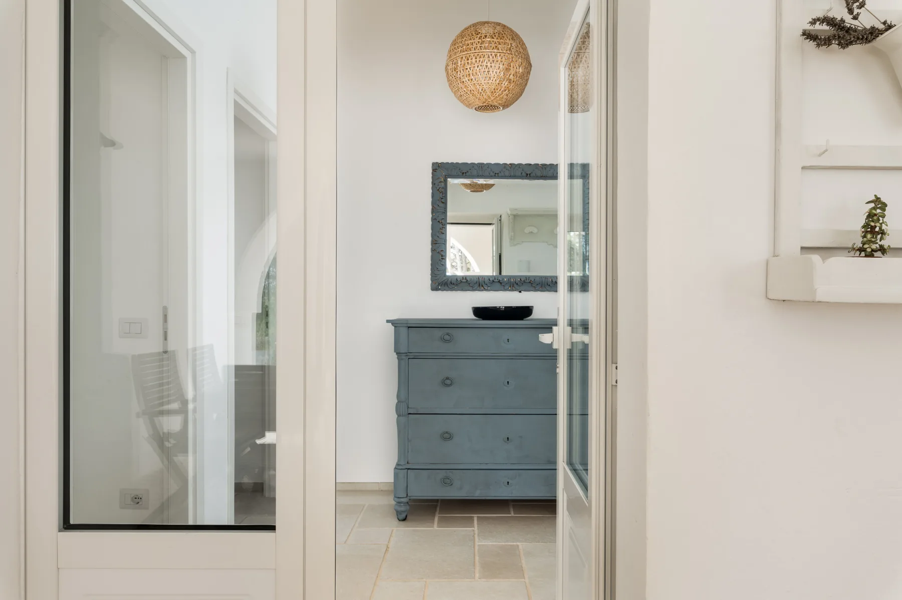 Un baño luminoso con un tocador azul grisáceo y un espejo de pared.