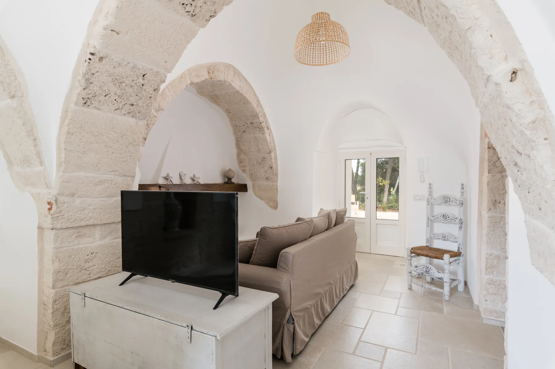 Una sala luminosa con televisor, asientos y techo de piedra con arcos.