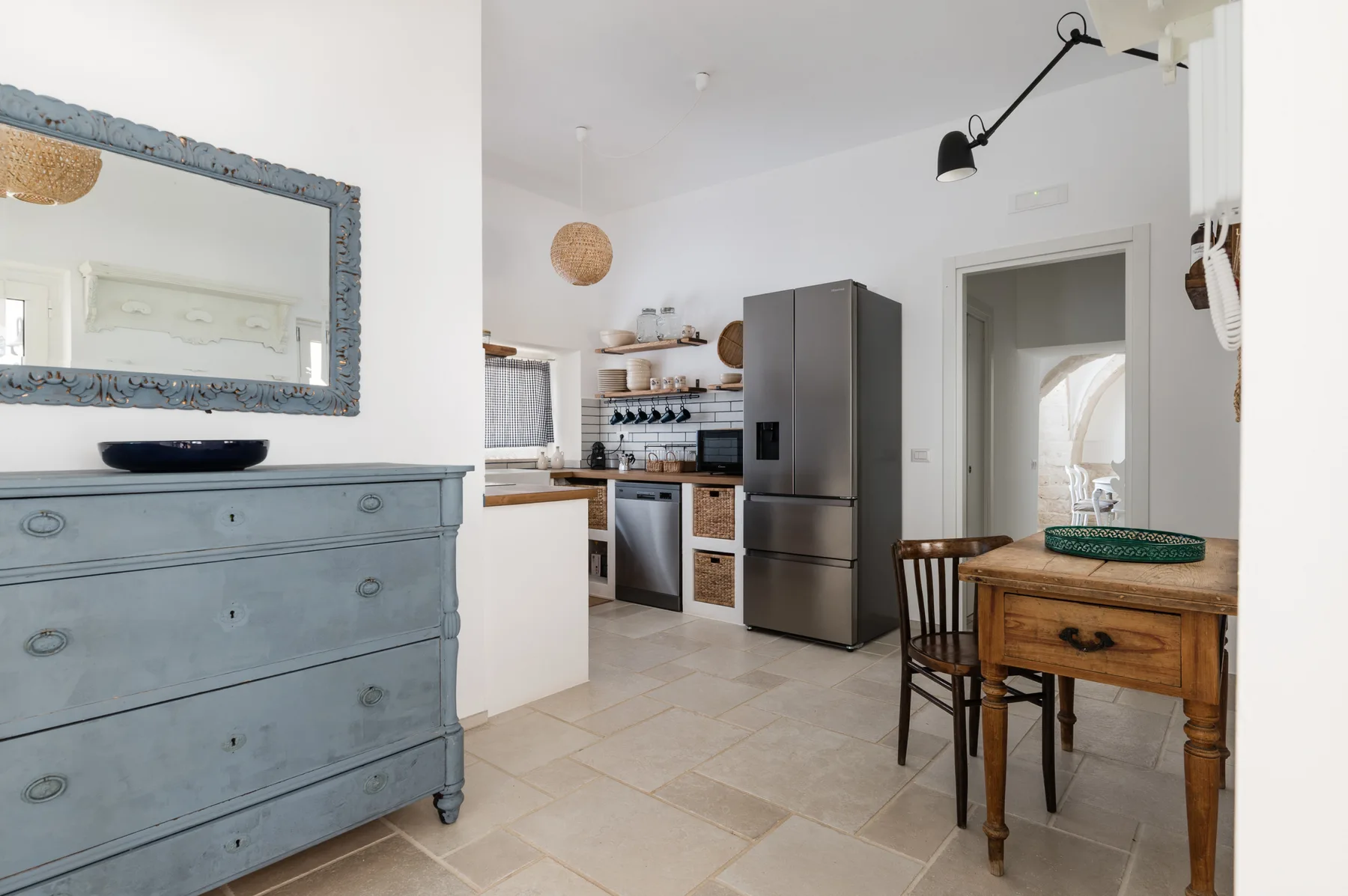 Una cocina luminosa con zona de comedor, mesa de madera y refrigerador gris.