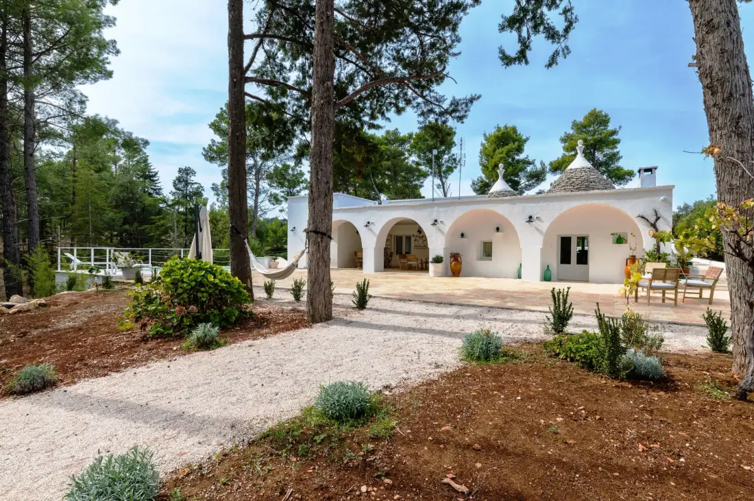 Una casa blanca con arcos está rodeada de altos pinos.
