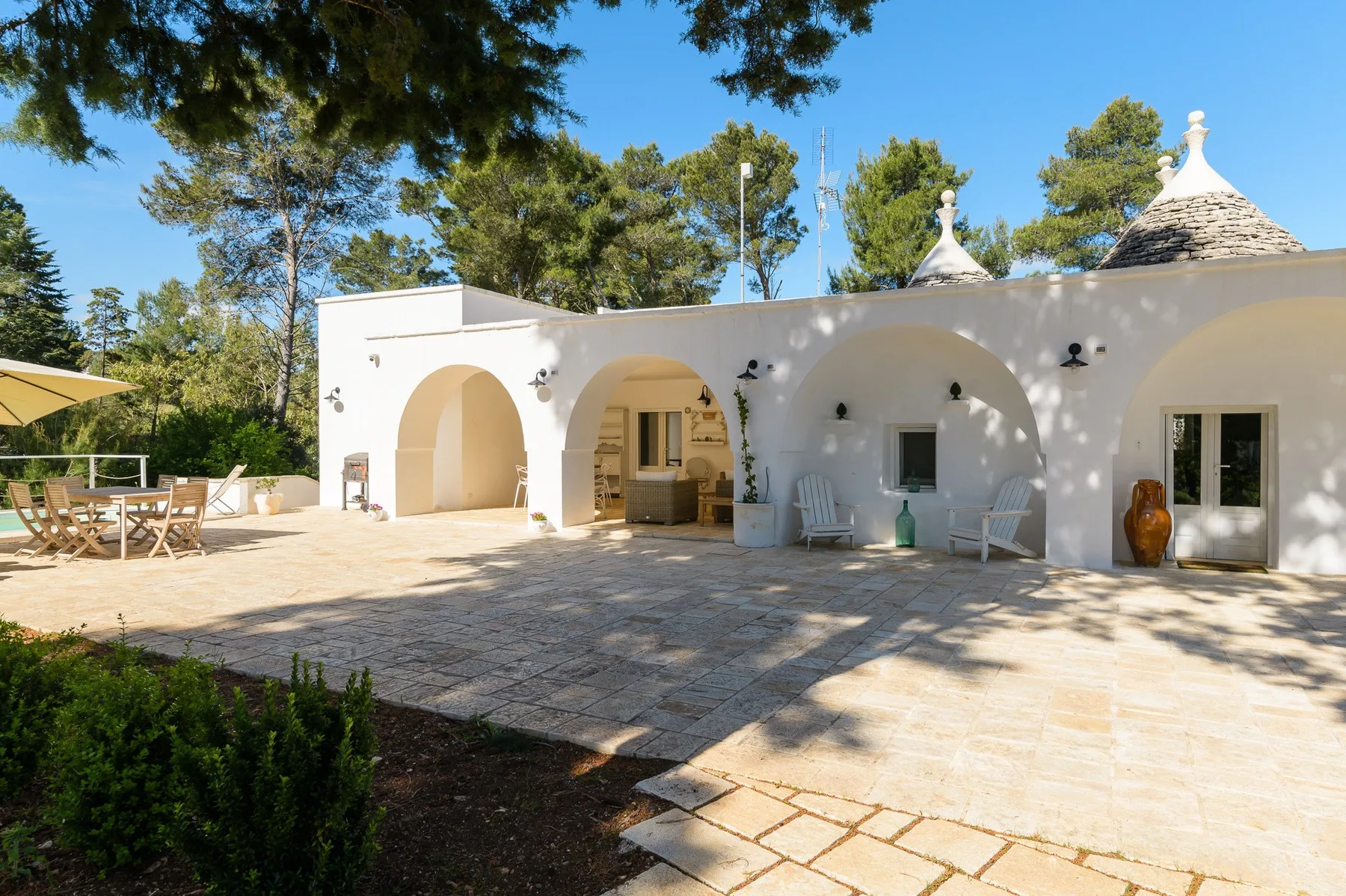 Un edificio blanco con arcos da a un patio soleado de piedra con asientos al aire libre.