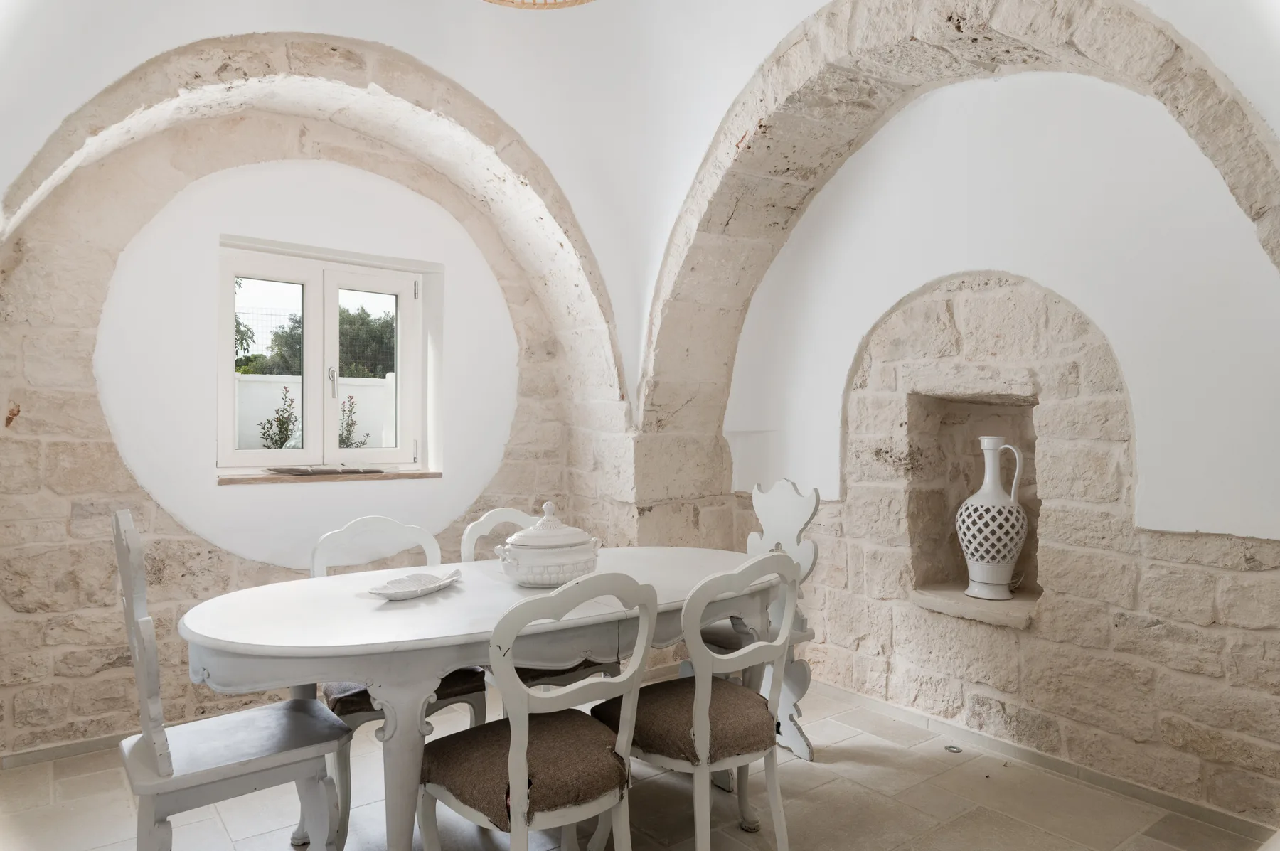 Un comedor con una mesa blanca y sillas bajo arcos de piedra.