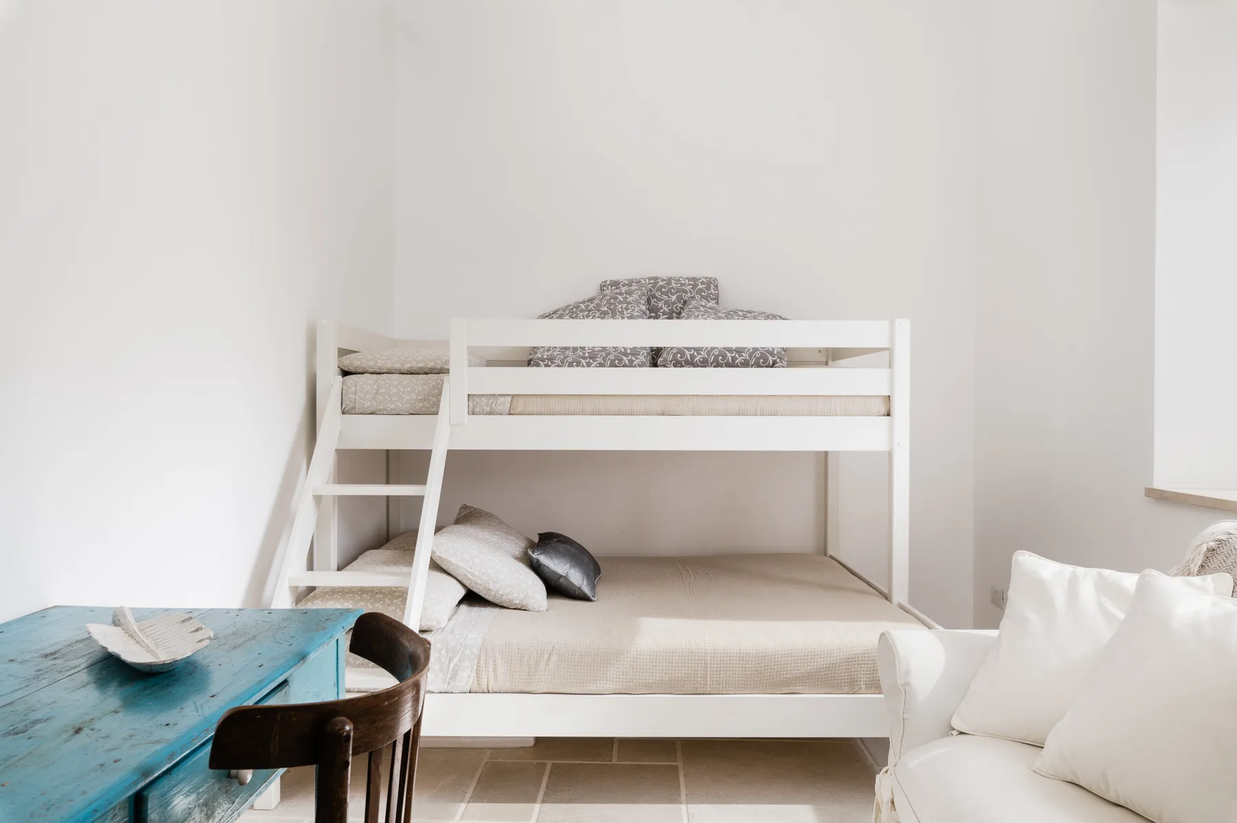 Un dormitorio luminoso con una litera blanca y una mesa turquesa.