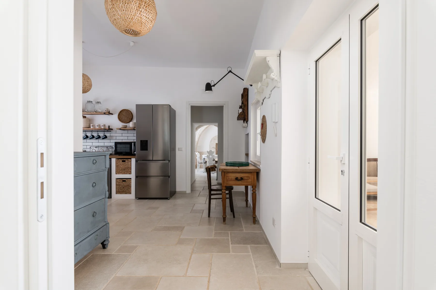 Una cocina luminosa con comedor, una mesa larga y un refrigerador de acero inoxidable.