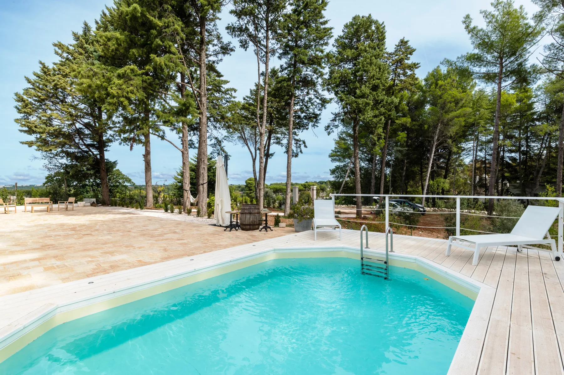 Una piscina al aire libre junto a una terraza de madera, rodeada de árboles.