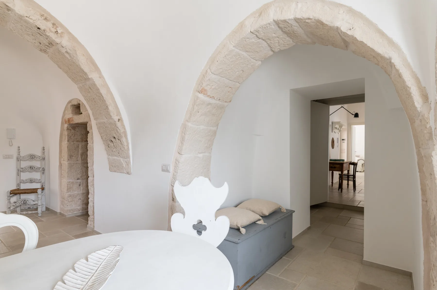 Un dormitorio luminoso con arcos de piedra y una cama junto a un banco con cojines.