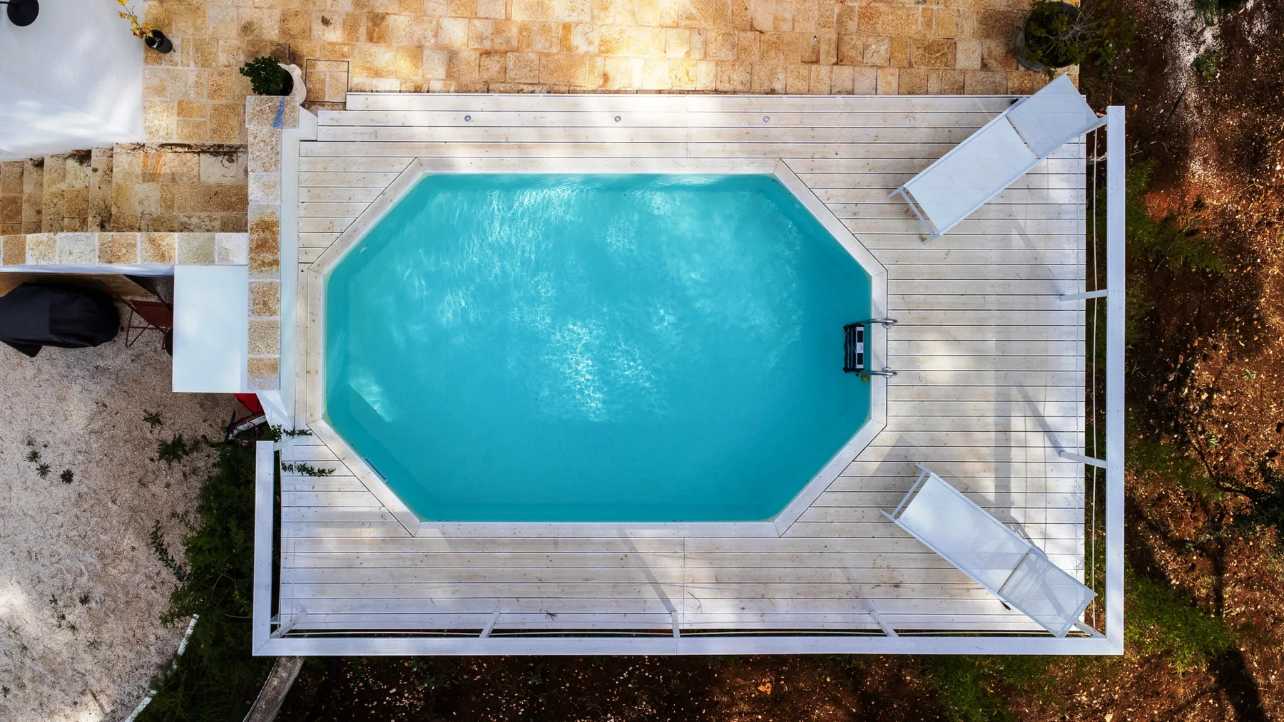 Una piscina al aire libre está rodeada por una terraza de madera y tumbonas.