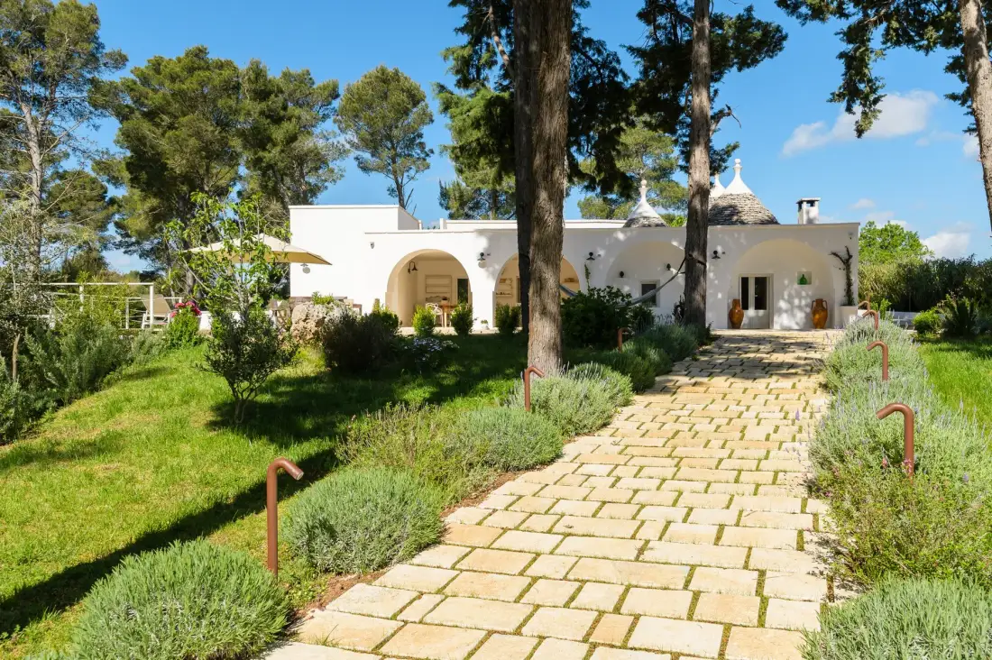 Un edificio blanco se encuentra al final de un camino de piedra entre jardines.