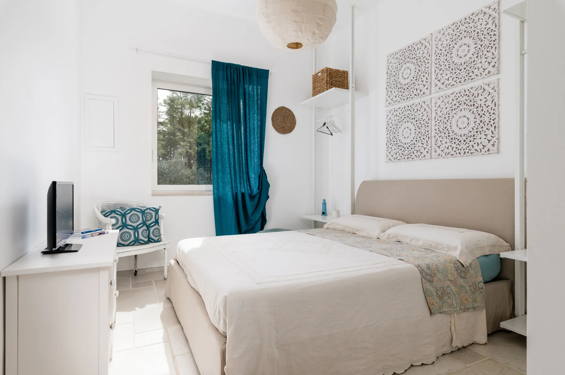 Un dormitorio luminoso con una cama doble, una ventana y cortinas turquesas.