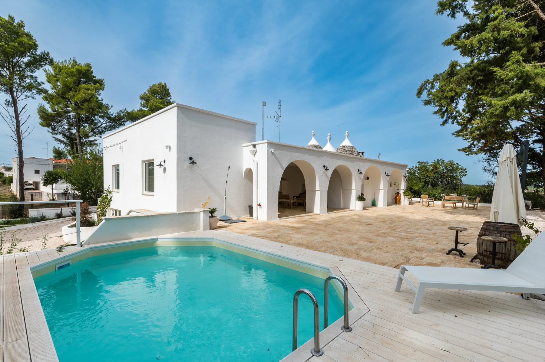 Una piscina junto a un edificio blanco con arcos y un patio pavimentado.
