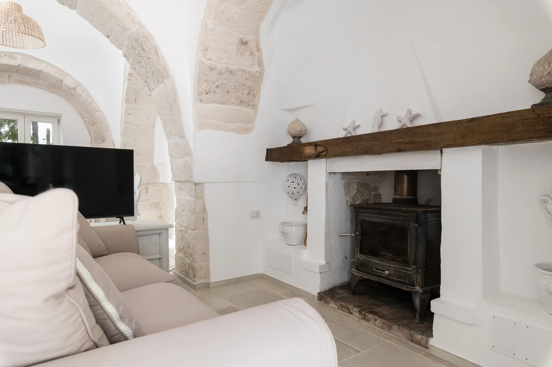Una sala de estar con asientos claros, un televisor y una chimenea bajo una repisa de madera.