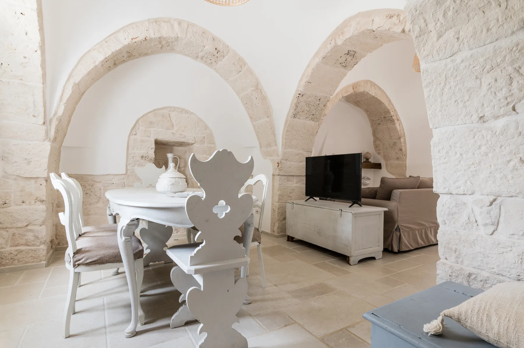 Un comedor con mesa y sillas está junto a arcos de piedra y un televisor.