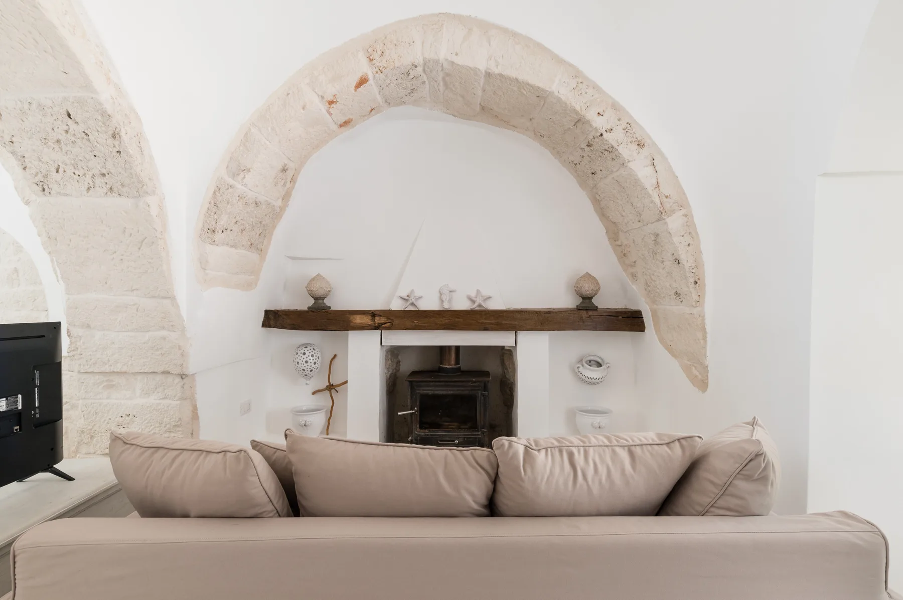 Una sala de estar con un sofá frente a una chimenea bajo un arco de piedra.