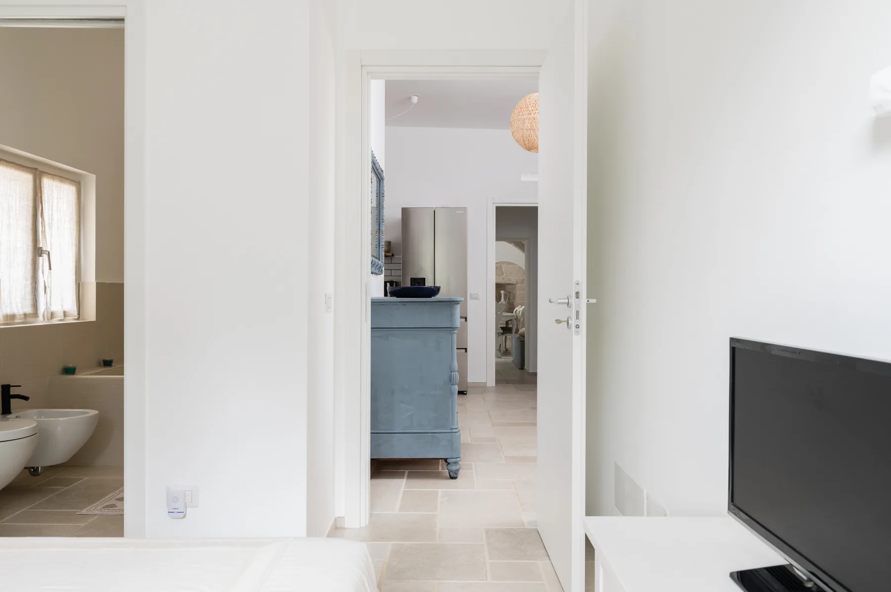 Un pasillo luminoso da a un mueble azul, con un baño visible a través de la puerta.