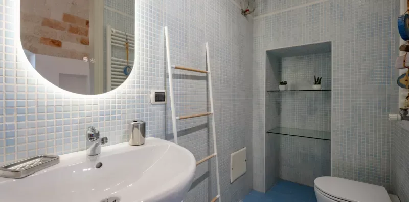 Un baño revestido de azulejos con lavabo, toallero tipo escalera y zona de ducha empotrada.