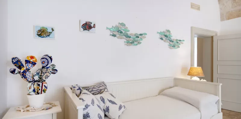 Un dormitorio luminoso con una cama blanca y adornos coloridos en la pared.