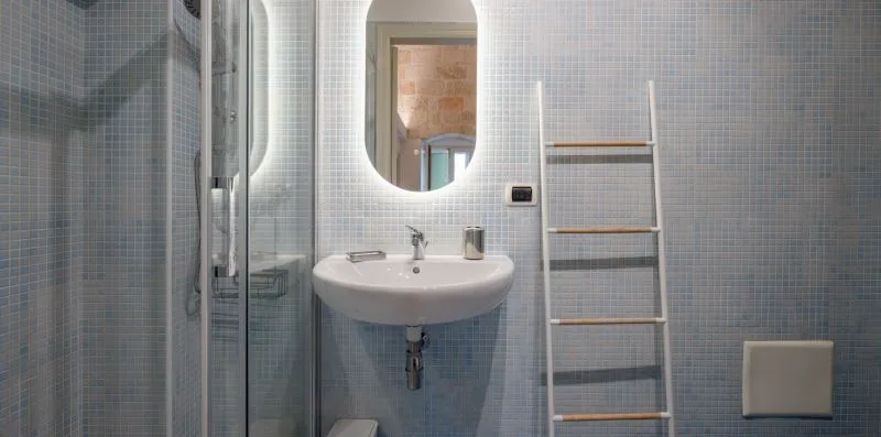 Un baño con azulejos, lavabo, espejo y ducha con mampara de vidrio.