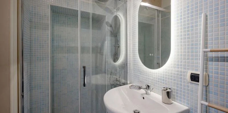 Un baño alicatado con ducha de cristal, espejo iluminado y lavabo.