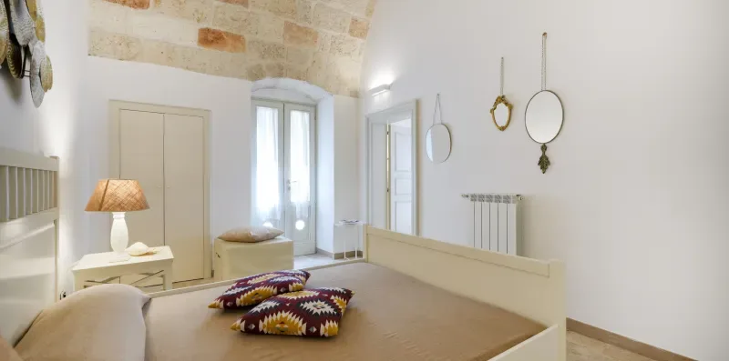 Un dormitorio luminoso con cama, mesita de noche y ventanas altas.