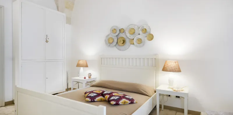 Un dormitorio luminoso con una cama blanca y cojines de colores estampados.