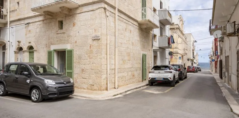 Una calle estrecha bordeada de edificios de piedra clara y coches estacionados.