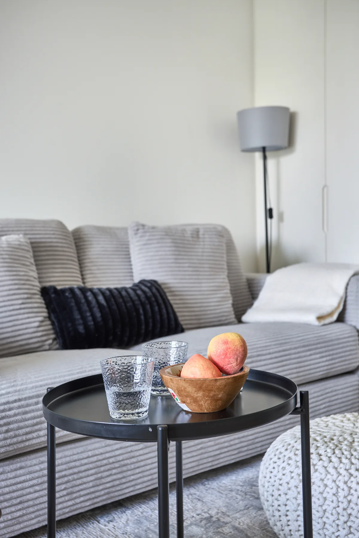 Una sala de estar con un sofá gris y una mesa redonda con fruta y agua.