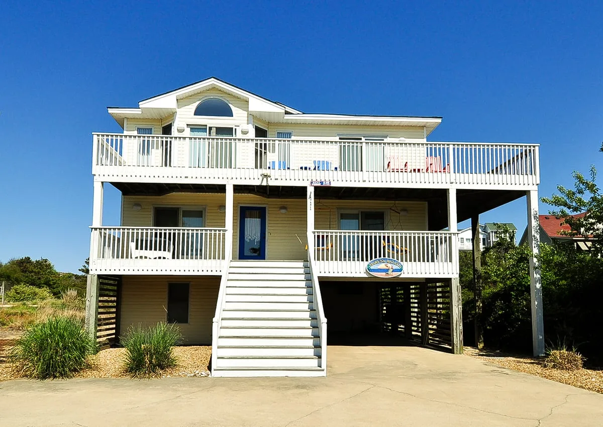 A raised coastal-style house with white railings and an exterior staircase.