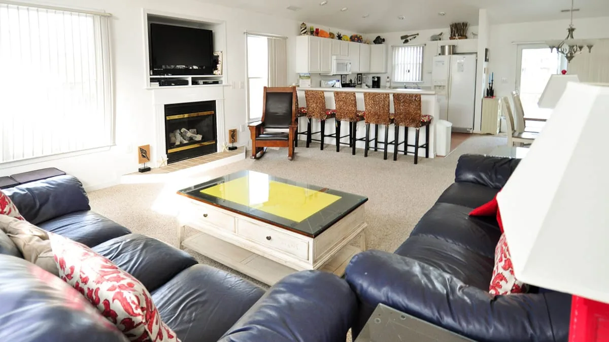 A living room opens onto a kitchen, with dark seating around a coffee table.